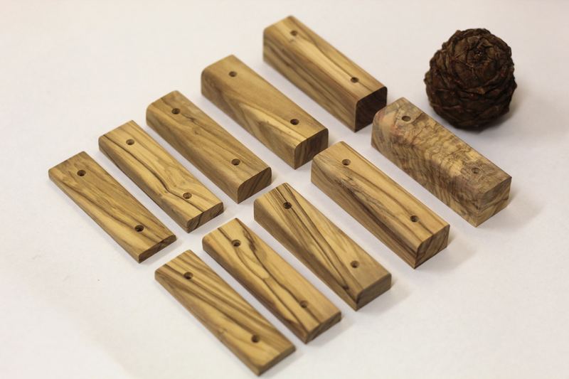 Set of 10 olive wood climbing edges with screw holes, next to a pine cone